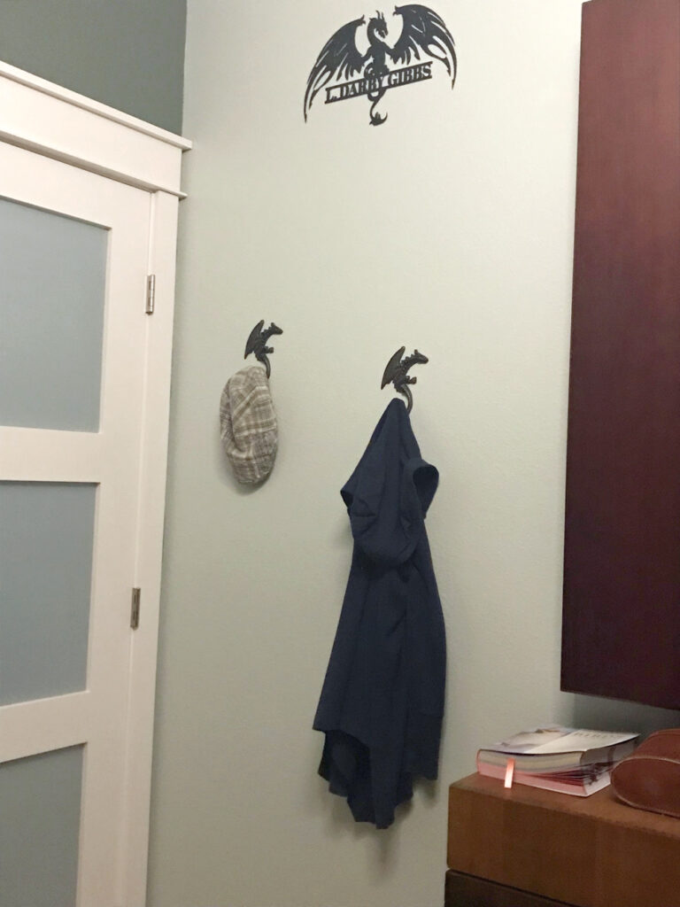 A dragon sign with the name L. Darby Gibbs and two dragon coat hooks hand on a wall.